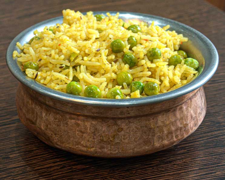 Fragrant yellow pilau rice with green peas in a rustic, copper serving bowl.